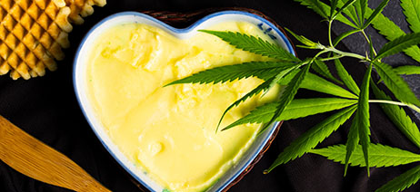 Cannabis butter in a heart shaped container with cannabis leaves over it