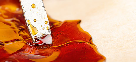 Dark amber puddle of live resin with a metal dab tool mixing it around