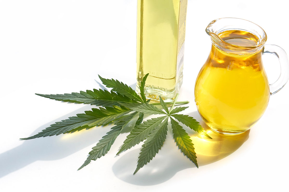 Two containers of cannabis cooking oil hovering over cannabis leaves