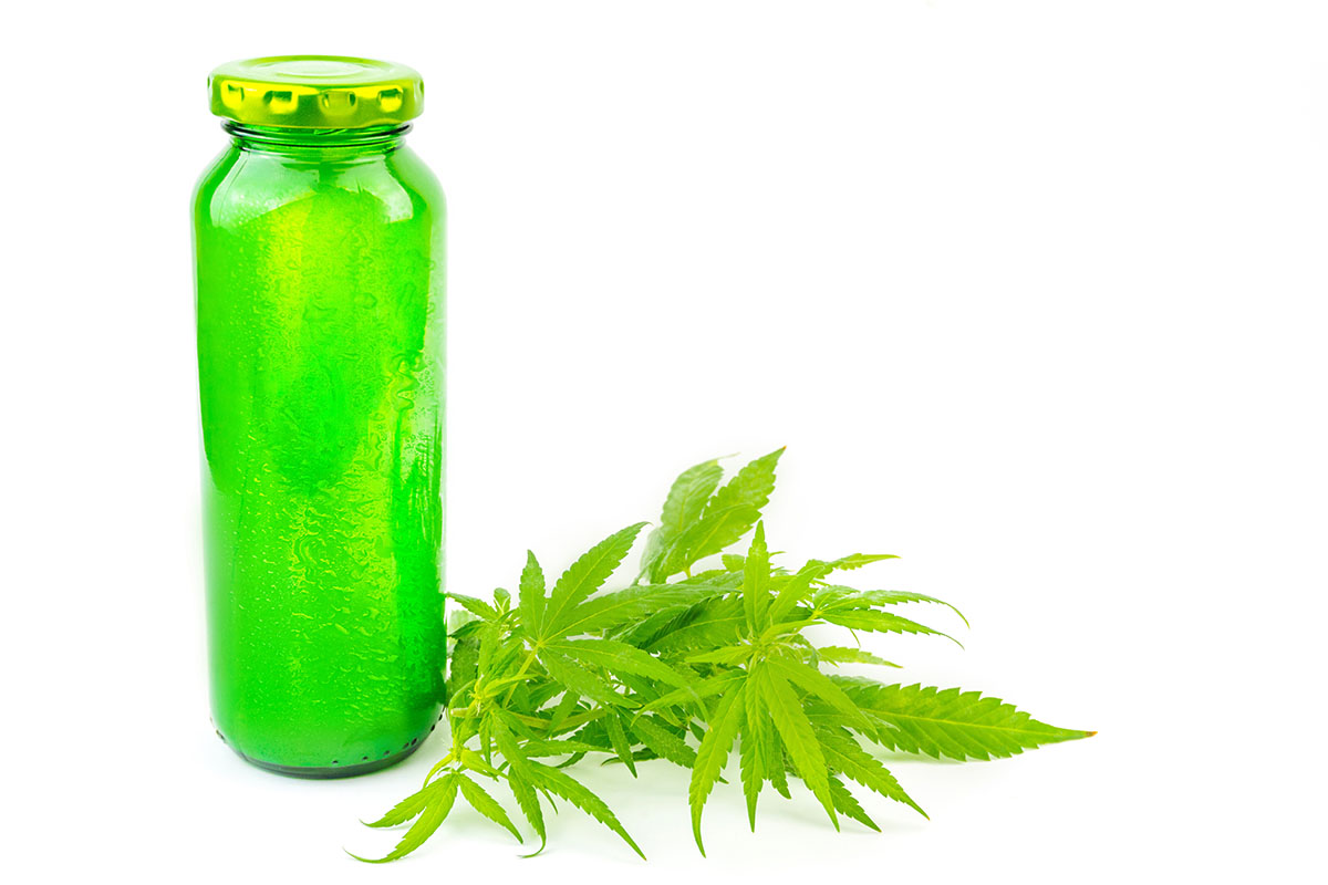 Bottle of green juice next to a pile of cannabis leaves