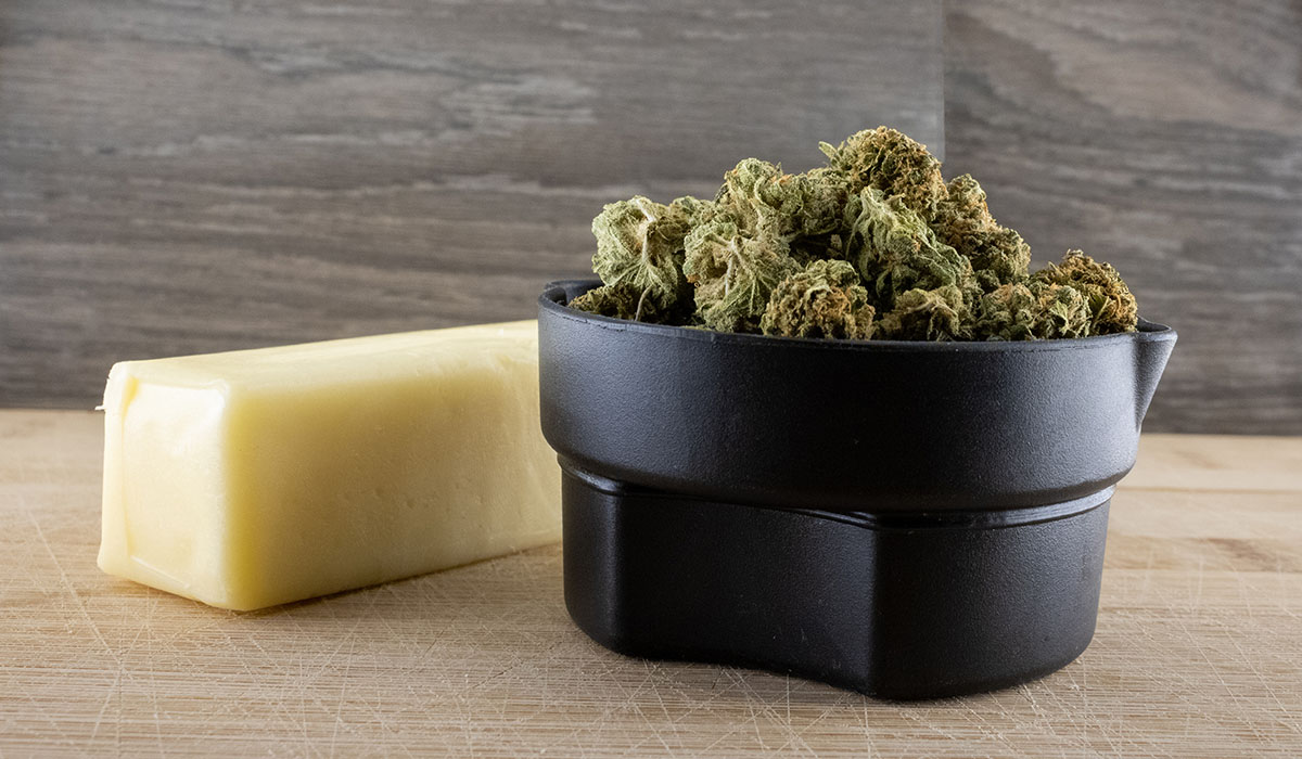 Cannabis flower in a black measuring cup next to a stick of butter