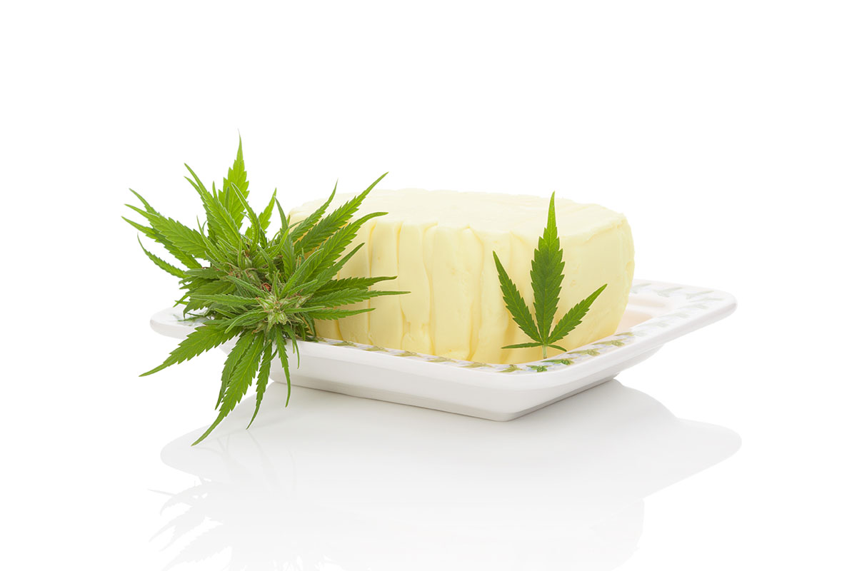 Stick of cannabis butter on a white plate with cannabis leaves surrounding it