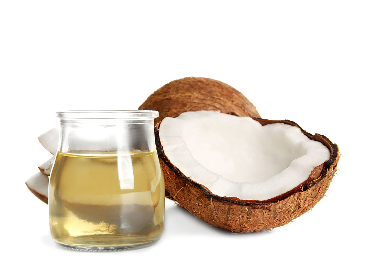 Half of a coconut cracked open next to a clear jar of oil