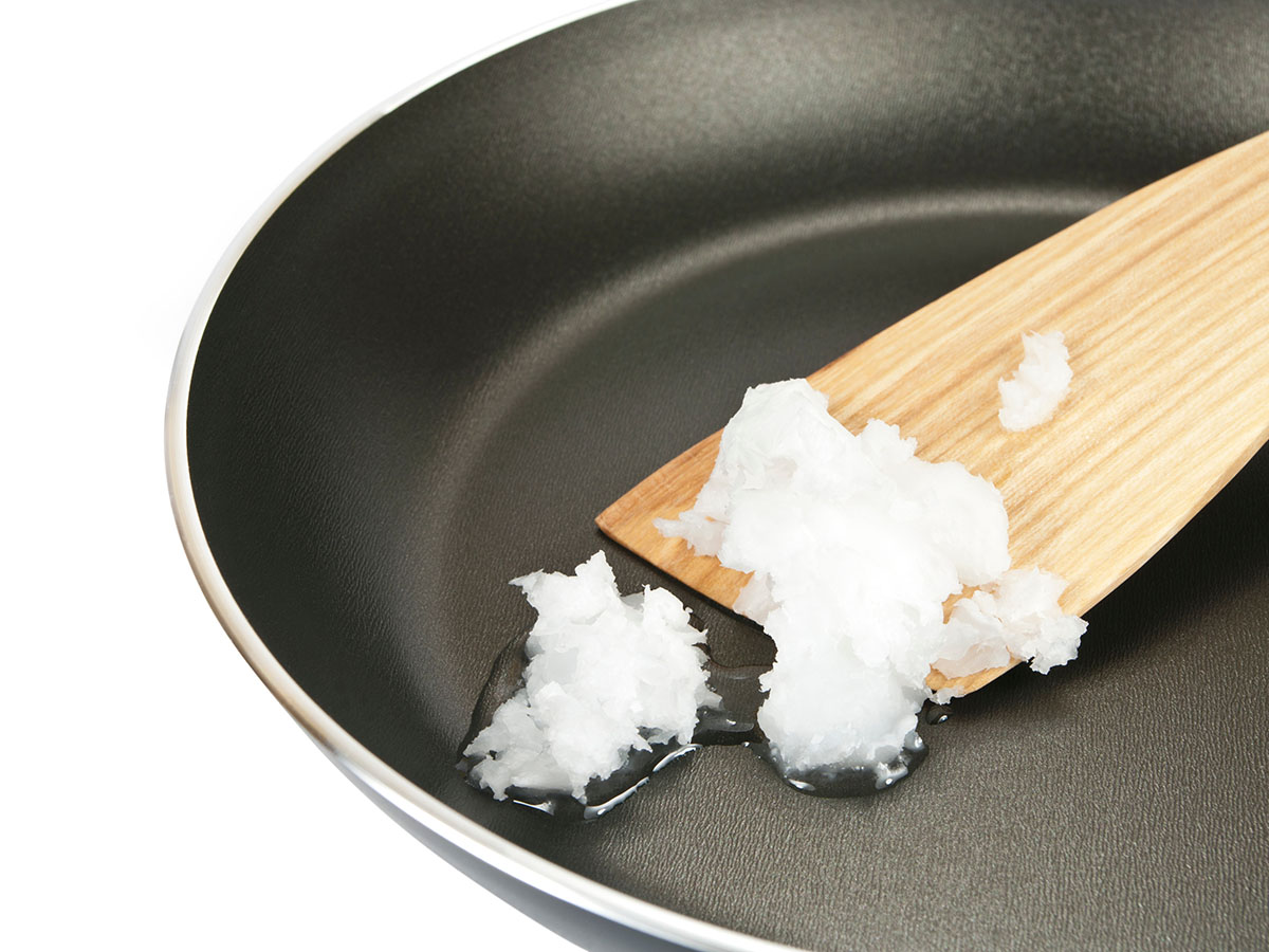 Coconut oil melting in a cooking pan with a wooden spatula mixing it around