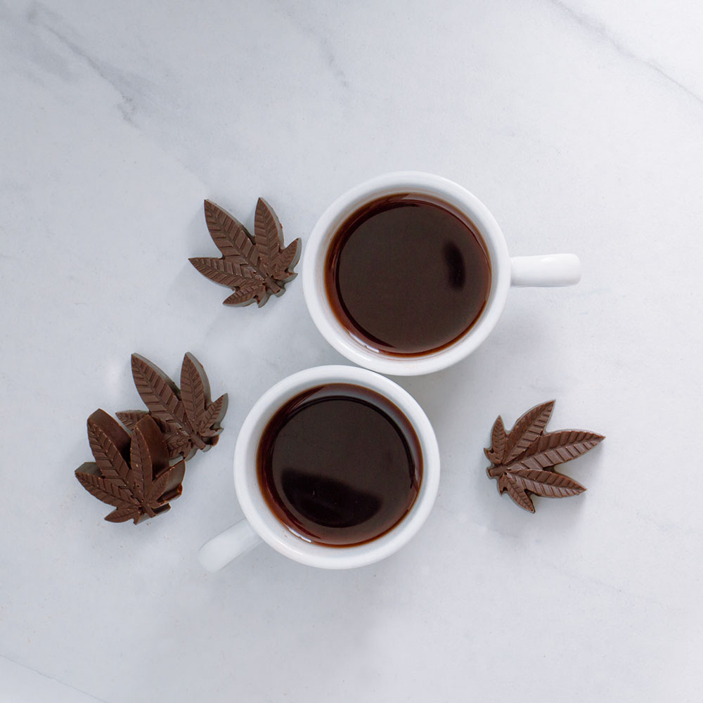 Two mugs of hot chocolate with chocolate candies in the shape of cannabis leaves