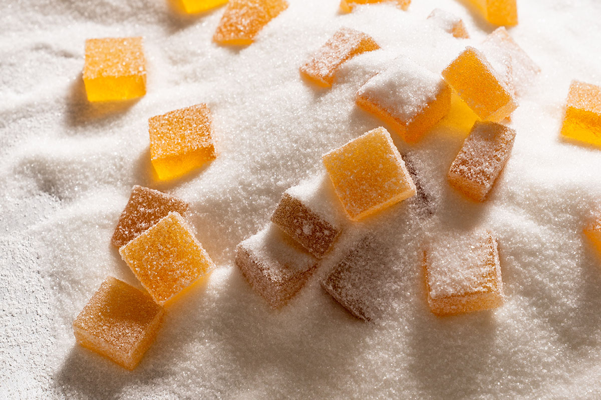 Square orange gummies being rolled in sugar