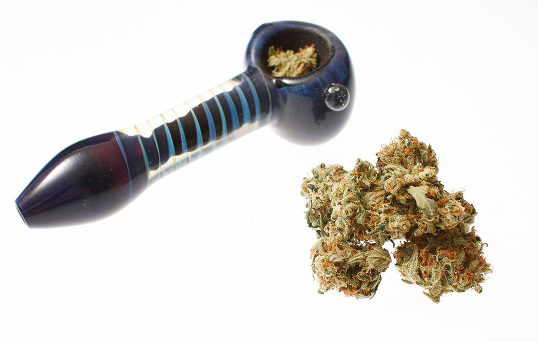 Dark blue glass cannabis hand pipe next to a large nugget of flower