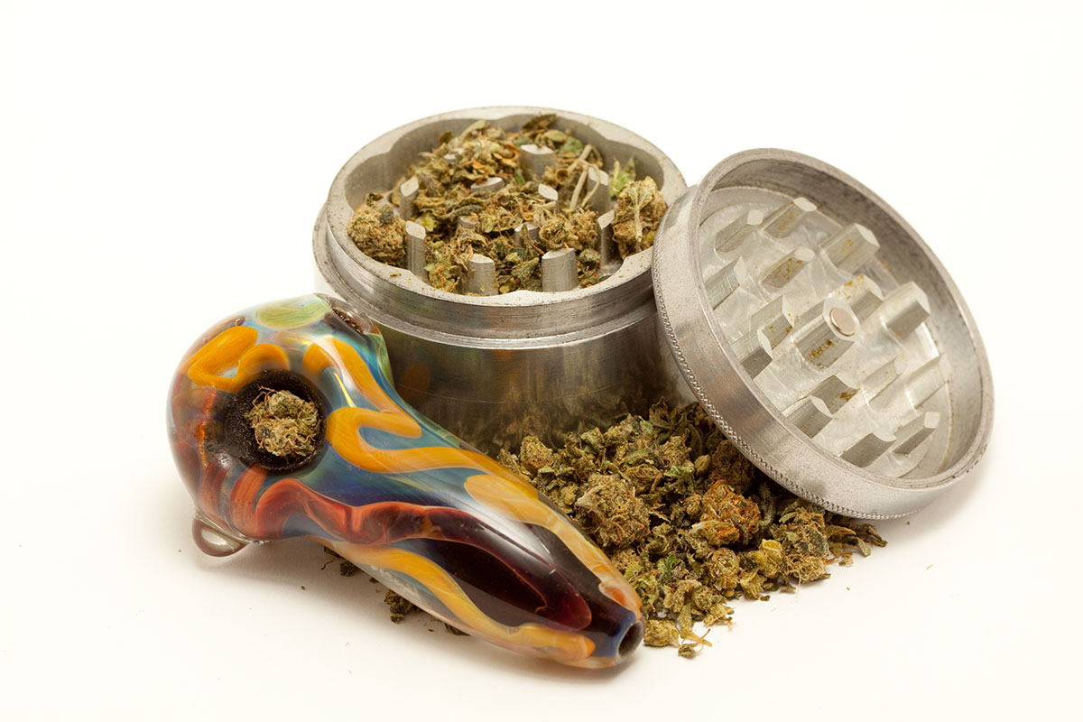 Cannabis grinder and pipe on top of a pile of ground flower