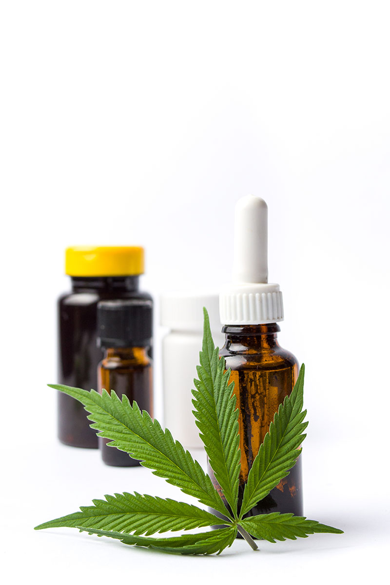 Cannabis tincture and tablet bottles grouped behind a marijuana fan leaf