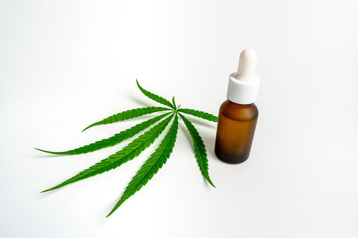 Brown tincture bottle in front of a cannabis fan leaf