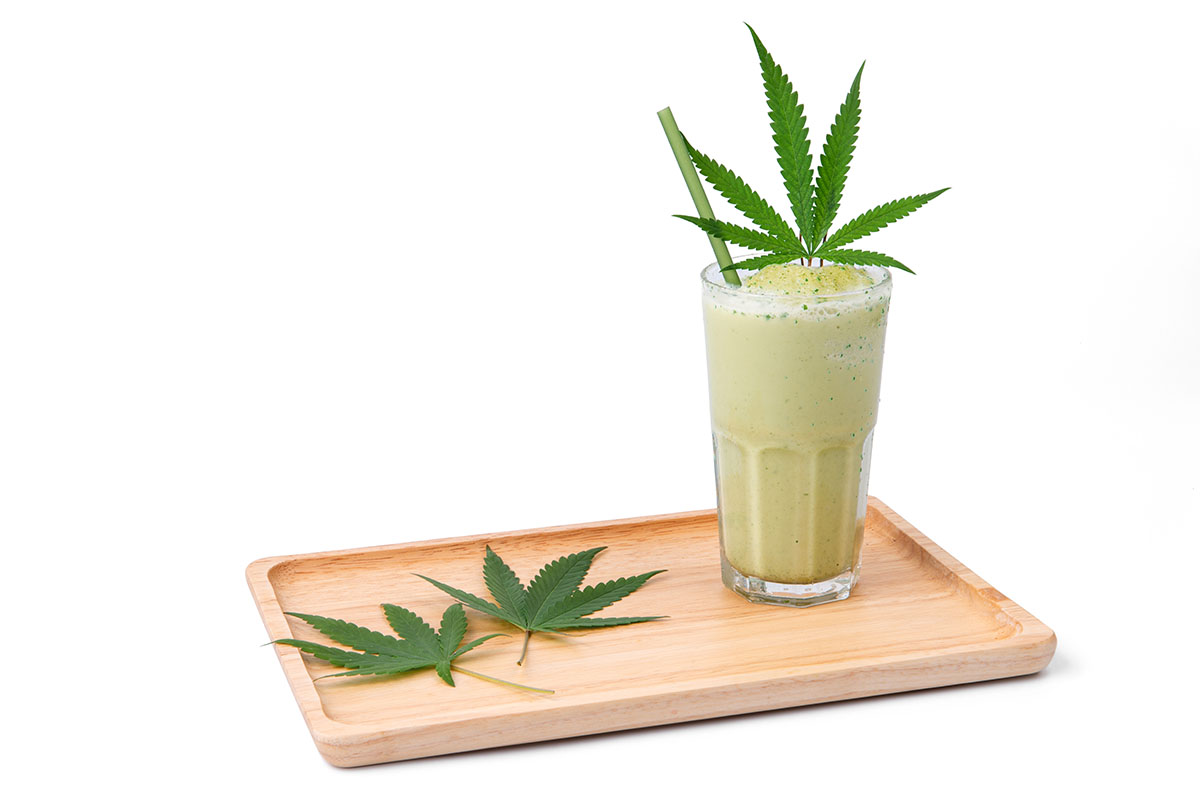 Smoothie in a glass with cannabis leaves on top, sitting on a wooden tray