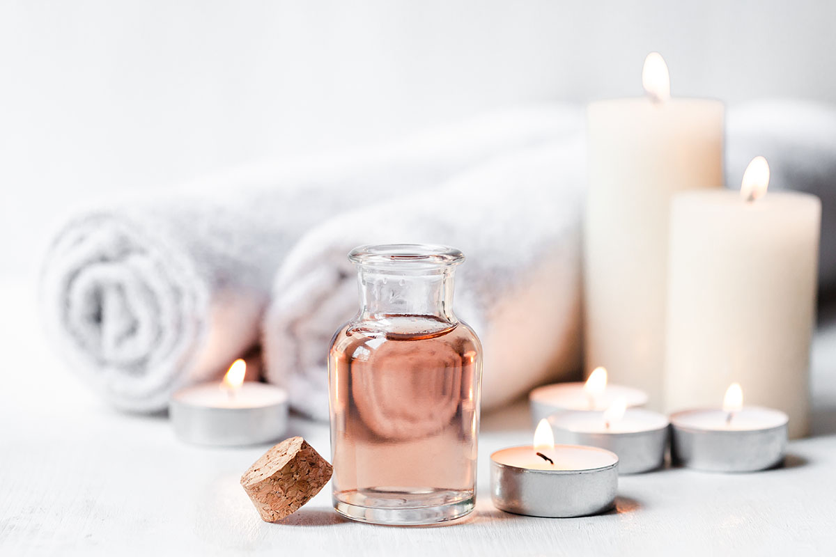 Pink oil bottle in front of candles and towels