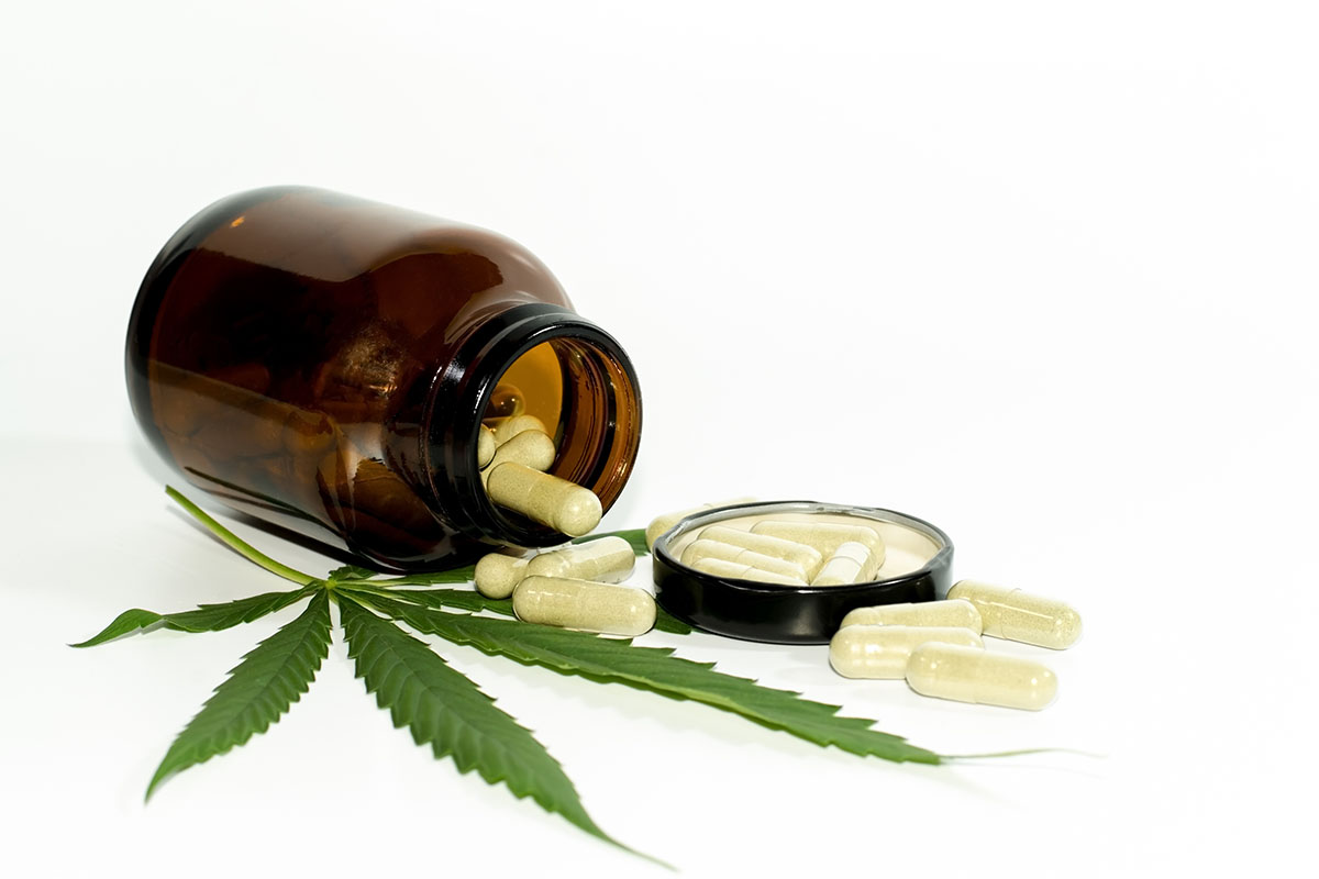 Pills spilling out of an opaque pill bottle onto a cannabis leaf