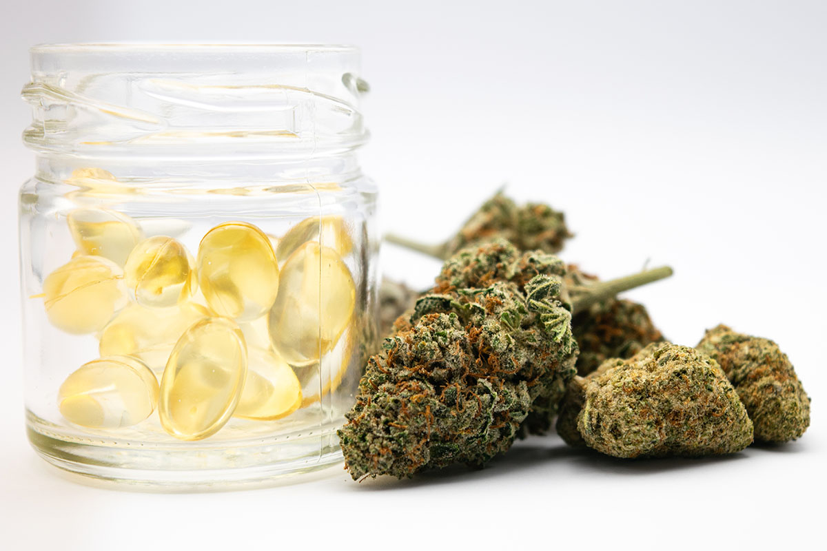 Gel caps in a small clear glass jar next to a pile of flower