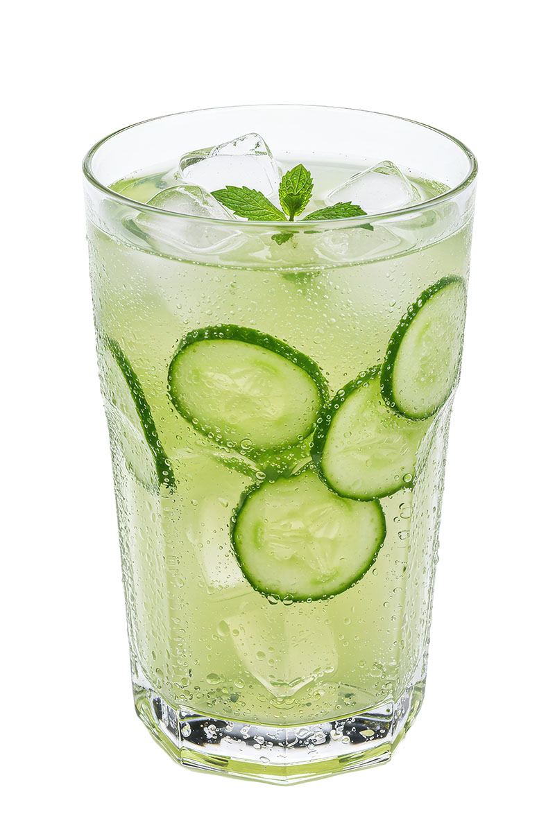 Fizzy green liquid in a clear glass with mint and cucumbers floating inside