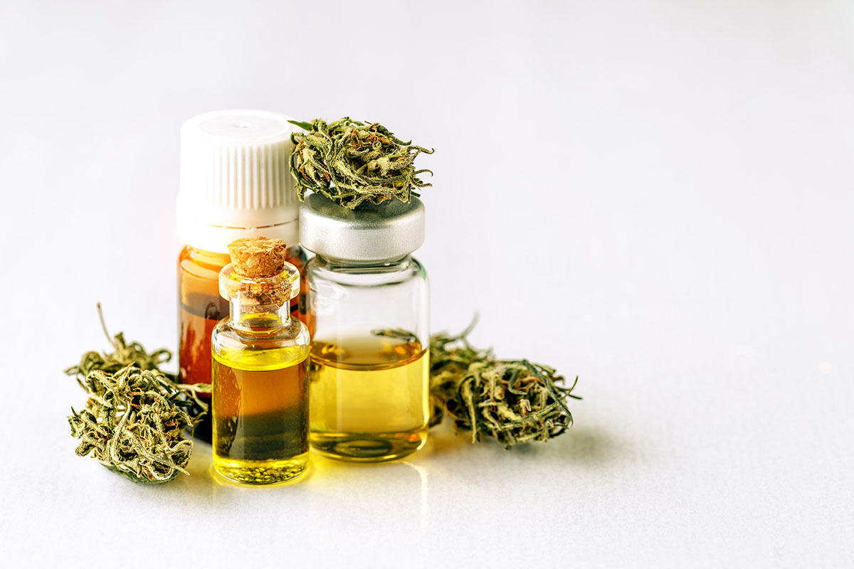Three small bottles of amber-colored oil next surrounded by cannabis buds