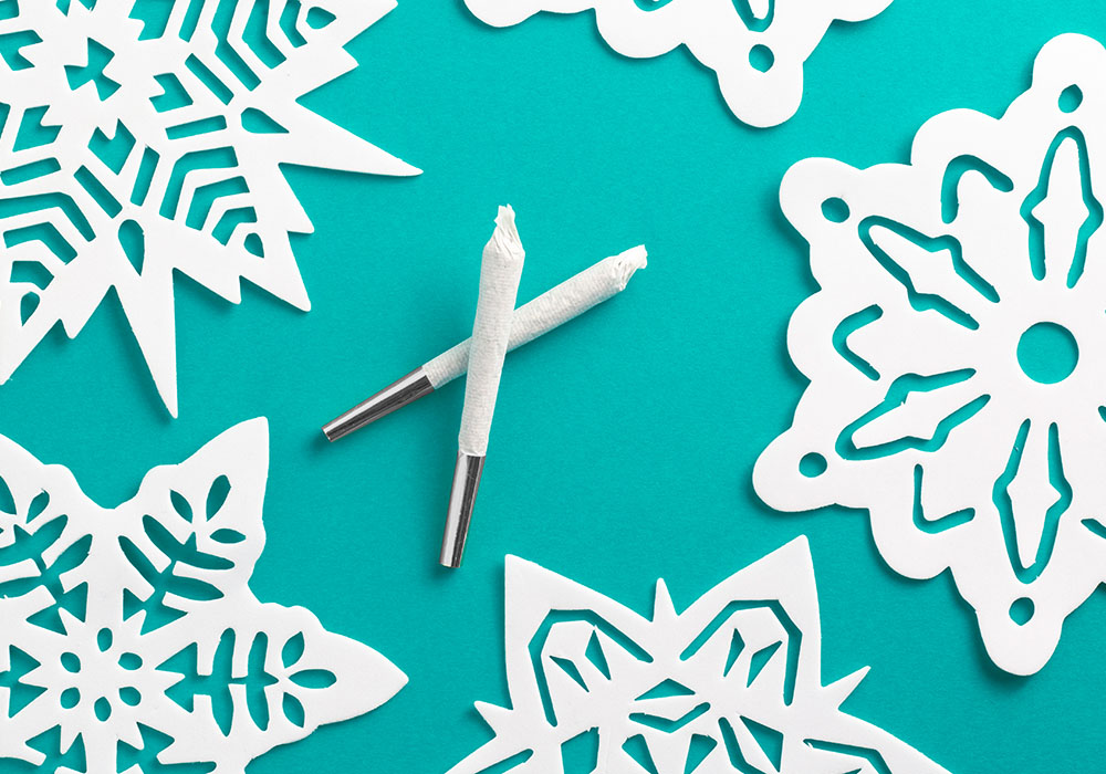 Two white joints with silver tips on a light blue background surrounded by paper snowflakes